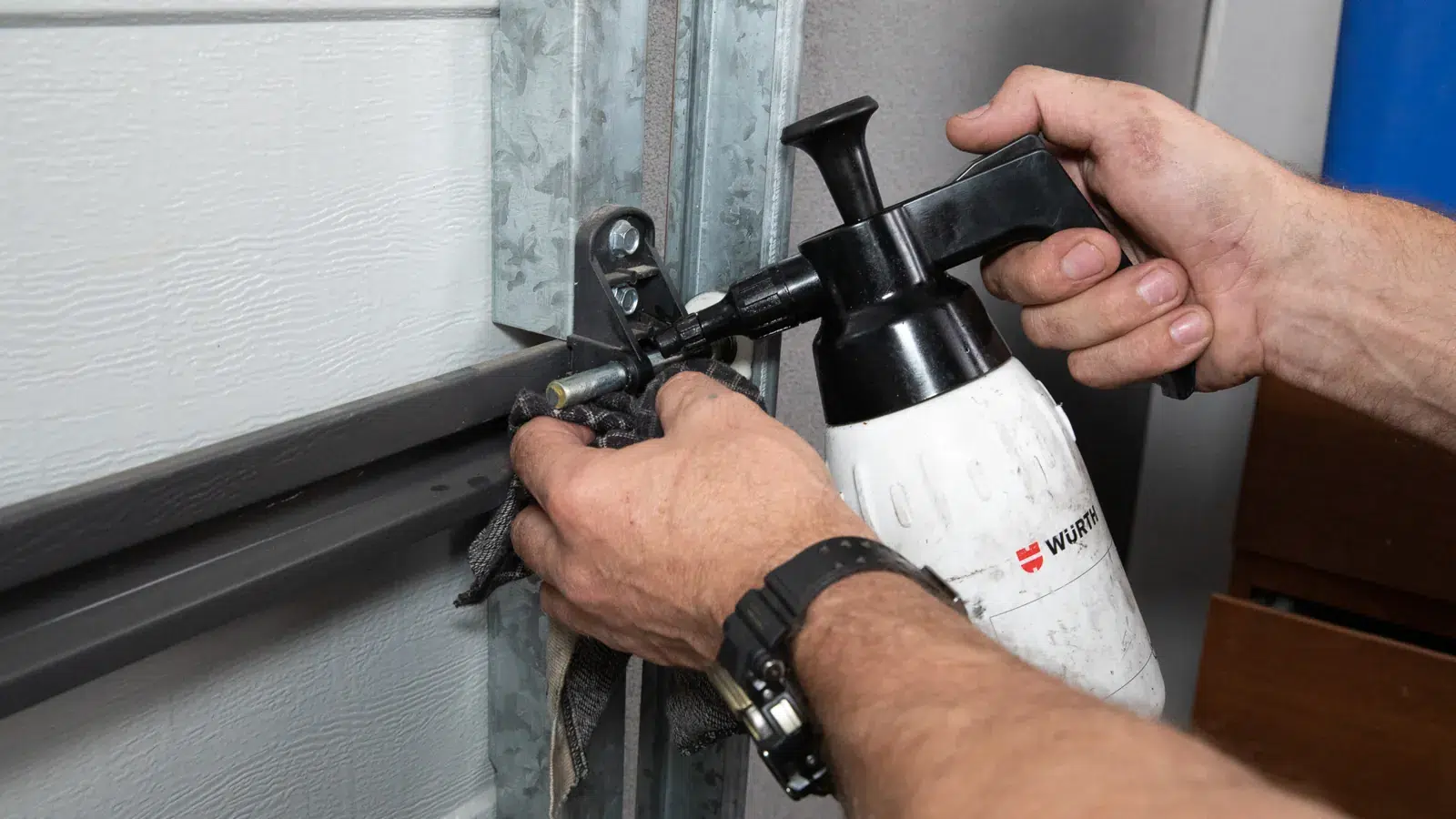 Technician cleaning and lubricating a garage door track