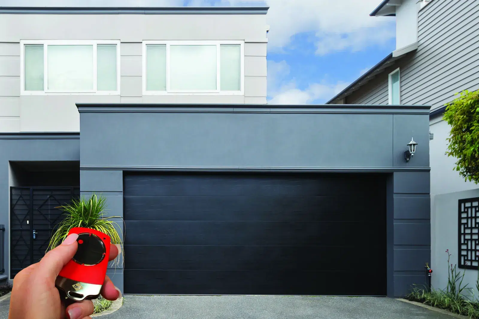 Hand holding a B&D remote in front of a dark Panelift Icon sectional garage door